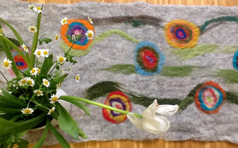 May include: A gray felt rug with a colorful abstract design. The design features multiple circles with concentric rings of different colors, including red, orange, yellow, green, blue, and purple. The rug is decorated with green and gray lines that resemble flowing water.