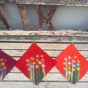 Könnte beinhalten: Drei handgefertigte Filz-Topflappen mit Blumenmuster. Die Topflappen sind rot, burgunderrot und orange mit grünen Stielen und bunten Blumen.