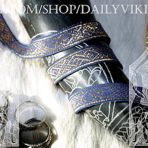 May include: A close-up of a black horn wrapped with blue and gold patterned ribbon. The ribbon has a geometric design. The text "ETSY.COM/SHOP/DAILYVIKING" is at the top of the image. The background is a white fur.