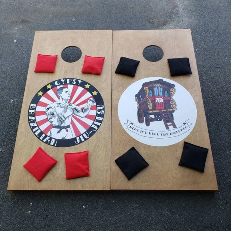 May include: Two wooden boards with a red and black design. The left board has a circle with the text "Gypsy Brazilian Jiu-Jitsu" and a man in a fighting pose. The right board has a circle with a wagon and the text "Home is where the mats are".