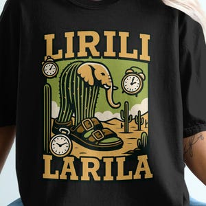 May include: Black t-shirt with a desert-themed graphic. The design features an elephant-shaped cactus, sandals, clocks, and the words "LIRILI LARILA" in a bold, vintage font. The shirt is a casual, unisex style.
