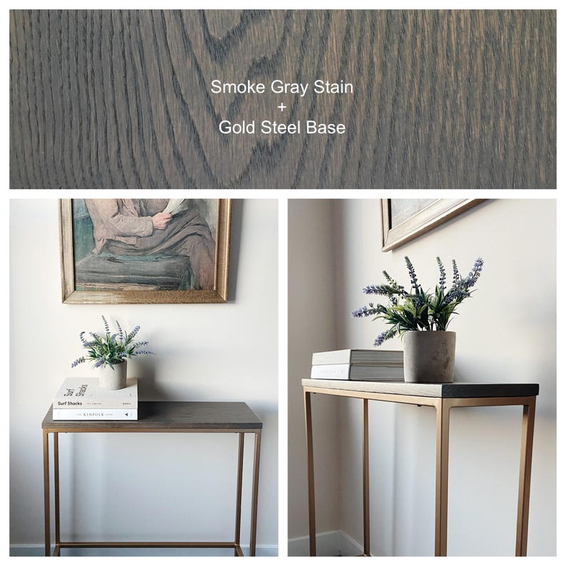 May include: A rectangular console table featuring a wood top with a smoke gray stain and a gold-colored steel frame. The text Smoke Gray Stain + Gold Steel Base is visible. The table is shown with books and a potted plant on its surface.