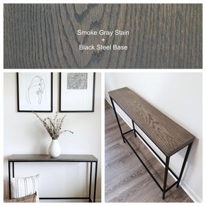 May include: A rectangular console table featuring a wood top with a smoke gray stain and a black steel base. The text Smoke Gray Stain + Black Steel Base is visible. The table has a slim, linear frame and a visible wood grain texture on the surface.