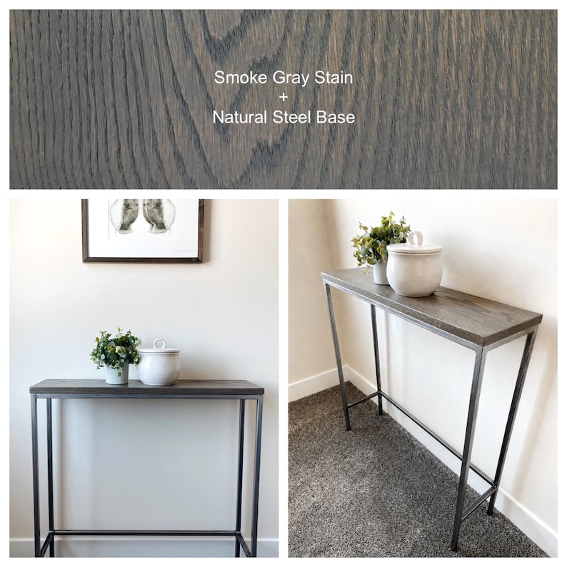 May include: A rectangular console table featuring a wood top with a smoke gray stain and a natural steel base. The text Smoke Gray Stain + Natural Steel Base is visible at the top. The table has a slim, tall frame with four straight legs.