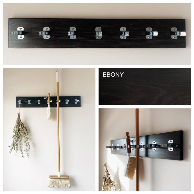 May include: A wall-mounted storage rack featuring a long, dark ebony-stained wooden board with seven silver metal spring-loaded clips attached. The rack is designed to hold cleaning tools like a broom and a brush, as shown in the demonstration.