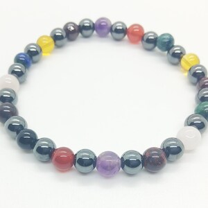 Könnte beinhalten: Ein Armband aus schwarzen Hämatitperlen mit bunten Edelstein-Akzenten. Das Armband zeigt eine Vielzahl von Farben, darunter Rot, Orange, Gelb, Grün, Blau, Lila und Weiß.