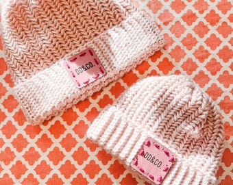 May include: Two pink knitted hats with a pink leather patch that says "DD&CO."