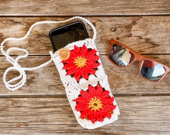 May include: White crocheted phone case with a red and yellow flower design. The case has a white strap and a brown "handmade" tag. Sunglasses are also in the image.