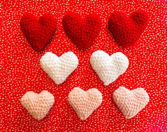 May include: Nine handmade crochet hearts in shades of red, white, and pink are arranged on a red background with white polka dots. The hearts are of varying sizes and textures, showcasing a handcrafted aesthetic.