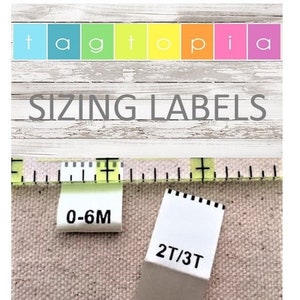 May include: Two white fabric clothing labels with black text. The label on the left says "0-6M" and the label on the right says "2T/3T".