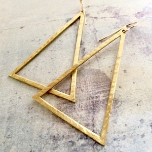 May include: A pair of gold triangle earrings with a hammered texture. The earrings are simple and modern in design.