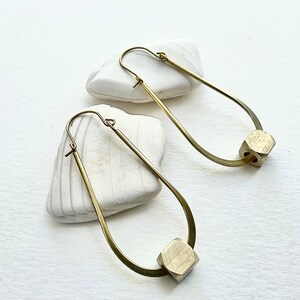 May include: A pair of gold hoop earrings with a geometric, hexagonal charm hanging from each hoop.
