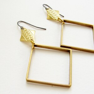 May include: A pair of gold-toned earrings with a geometric square design. Each earring features a small, textured diamond-shaped piece at the top.