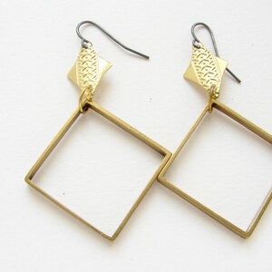 May include: A pair of gold-toned earrings with square frames and a textured diamond-shaped pendant on each earring.
