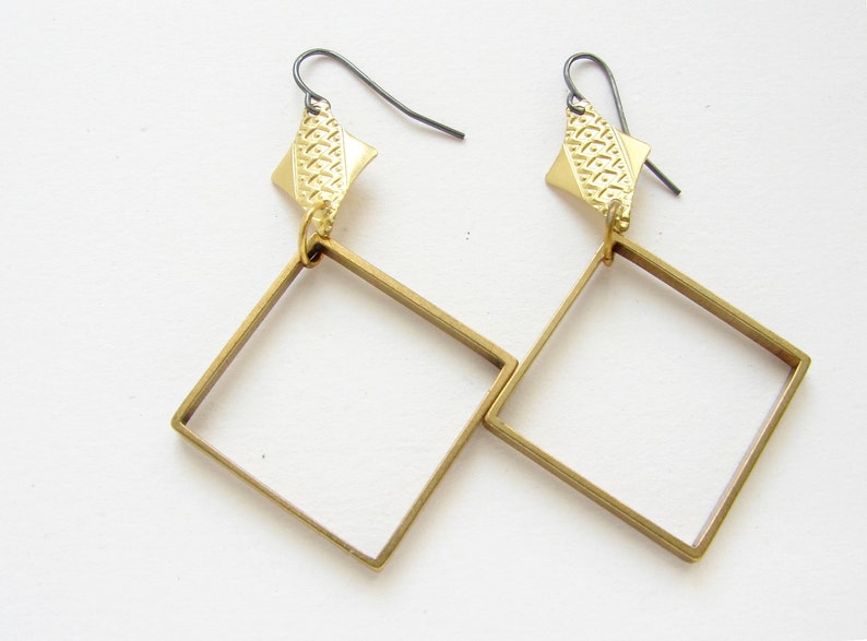 May include: A pair of gold-toned earrings with square frames and a textured diamond-shaped pendant on each earring.
