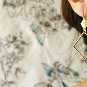 May include: Gold-toned geometric earrings with a square shape and a smaller, textured detail at the top.