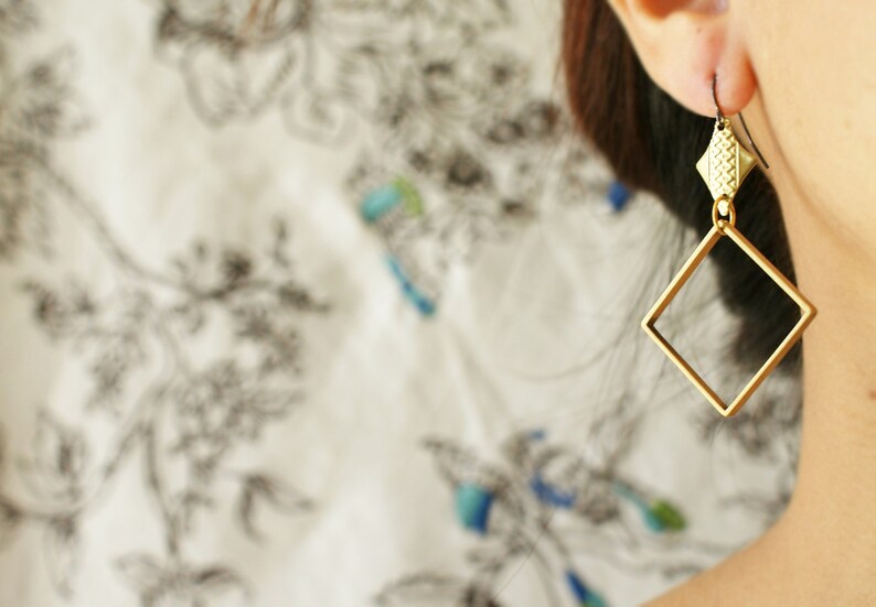 May include: Gold-toned geometric earrings with a square shape and a smaller, textured detail at the top.