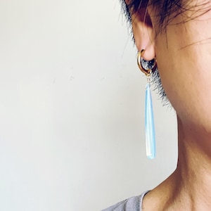 May include: A gold hoop earring with a long, teardrop-shaped blue and white glass dangle.