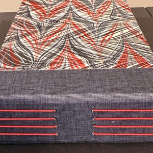 May include: A rectangular box with a marbled pattern top in red, black, and white. The bottom section is a dark blue fabric with four horizontal red stitches. The box is likely for storage or display.