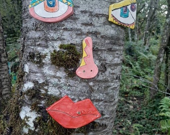 Puede incluir: Un tronco de árbol con una cara pintada de azulejos de cerámica. La cara tiene dos ojos, una nariz y una boca. Los ojos son azules, verdes y amarillos. La nariz es naranja y rosa. La boca es roja.