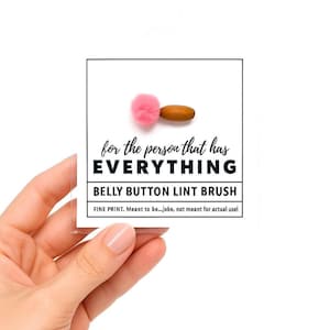 May include: A novelty belly button lint brush with a pink fluffy end and a wooden handle. The text on the card reads "for the person that has EVERYTHING" and "BELLY BUTTON LINT BRUSH".