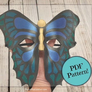 May include: A butterfly mask with a black base, blue and teal accents, and a gold center. The mask has eye cutouts and a black elastic strap. The text "PDF Pattern!" is in a teal circle.