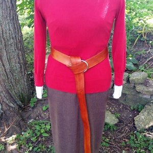 May include: A red sweater with a brown leather belt and a brown skirt.