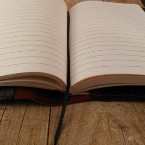 May include: A brown leather-bound journal with a black ribbon bookmark. The journal has lined pages and is open to a blank page.