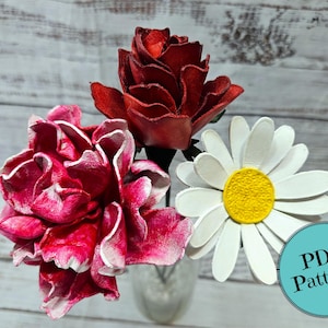 May include: A bouquet of handmade paper flowers in a clear vase. The arrangement includes a red rose, a pink peony, and a white daisy with a yellow center. A teal circle with the text "PDF Pattern!" is in the image.
