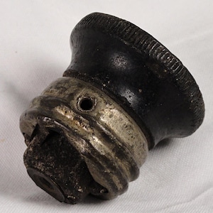 May include: A black and silver bottle stopper with a textured, rounded top and a detailed metal base. The stopper has a cylindrical shape and appears to be made of metal and possibly wood or a similar material.