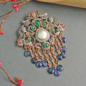 May include: A silver and gold pendant with a pearl and green, blue, and pink gemstones. The pendant has a detailed design and hangs from a chain of blue and pink gemstones.