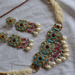 May include: A gold necklace and earrings set with turquoise and red stones, white pearls, and pink beads. The necklace has a choker style with a decorative pendant.