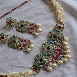 May include: A turquoise and gold necklace with red and pink stones, and pearl accents. The necklace is paired with matching earrings.