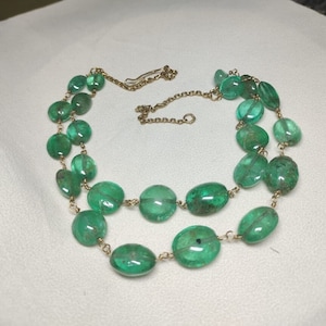 May include: A double strand necklace made of oval-shaped emerald green gemstones connected by a gold chain.