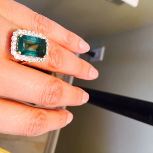 May include: A gold ring with a large emerald green gemstone surrounded by smaller diamonds.