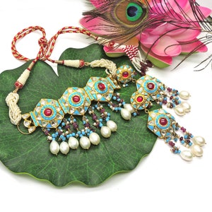 May include: A turquoise and gold necklace with red and white stones, featuring a central pendant with a floral design and dangling pearl and turquoise beads.