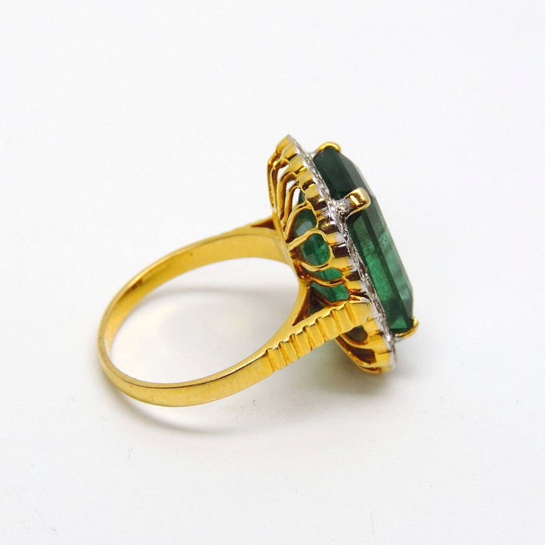 May include: A gold ring with a large, emerald green gemstone surrounded by smaller diamonds. The ring has a delicate, ornate design.