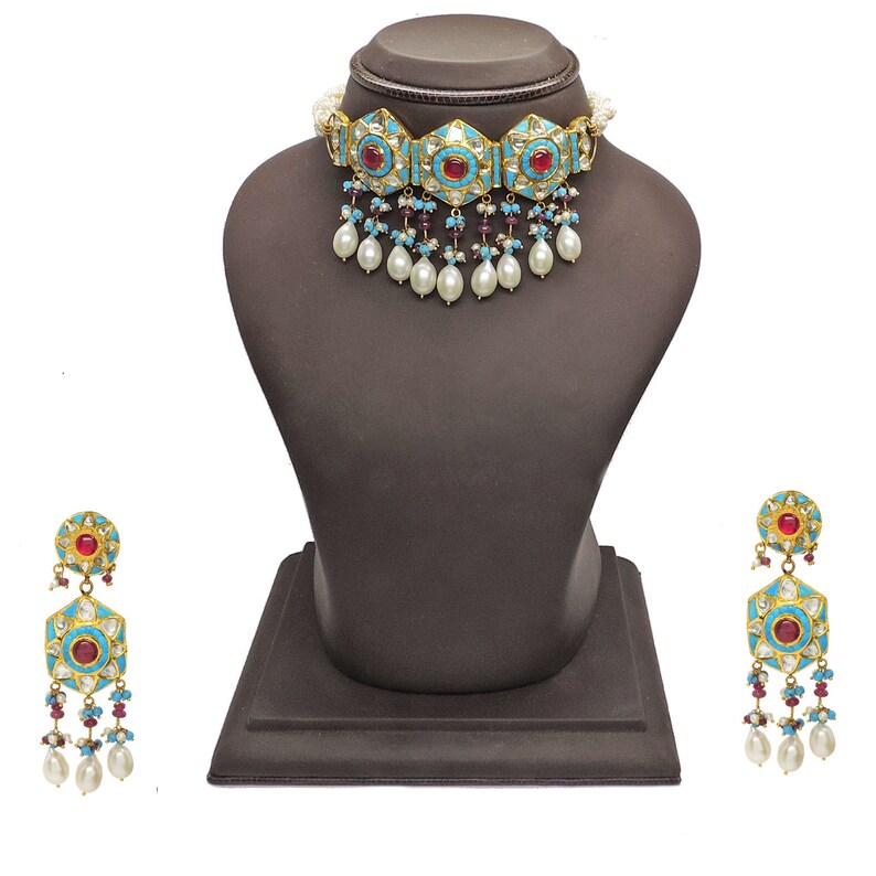 May include: A gold choker necklace with turquoise and red stones, pearl drops, and matching earrings. The necklace and earrings are on a black display stand.