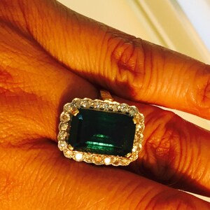 May include: A gold ring with a large emerald green gemstone surrounded by a halo of smaller diamonds.