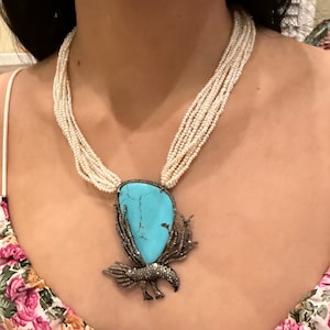 Puede incluir: Un collar de perlas de múltiples hilos con un colgante de turquesa y diamantes con un diseño de pájaro.