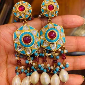 May include: A pair of gold earrings with turquoise and red stones, and pearl drops. The earrings have a floral design and are decorated with small diamonds.