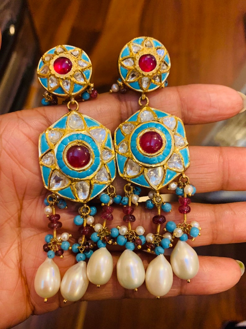 May include: A pair of gold earrings with turquoise and red stones, and pearl drops. The earrings have a floral design and are decorated with small diamonds.