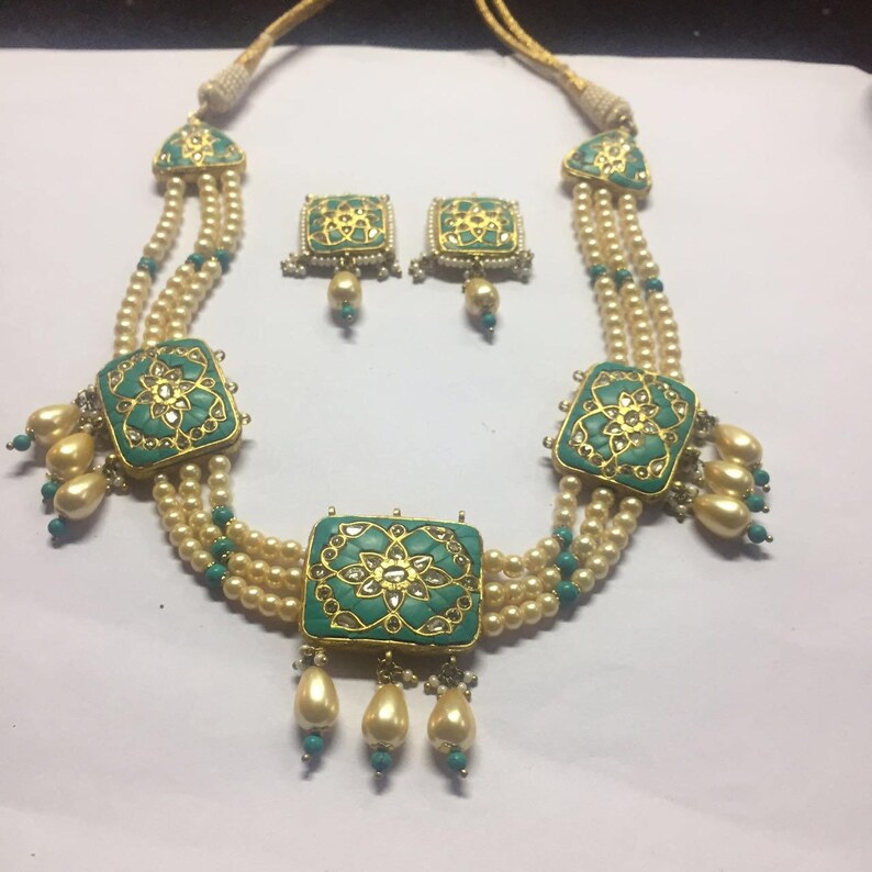 May include: A three-strand pearl necklace with green and gold square pendants. The necklace has a matching pair of earrings with green and gold square designs.
