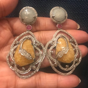 May include: A pair of silver earrings with a yellow and white gemstone, a white gemstone, and a pink gemstone.