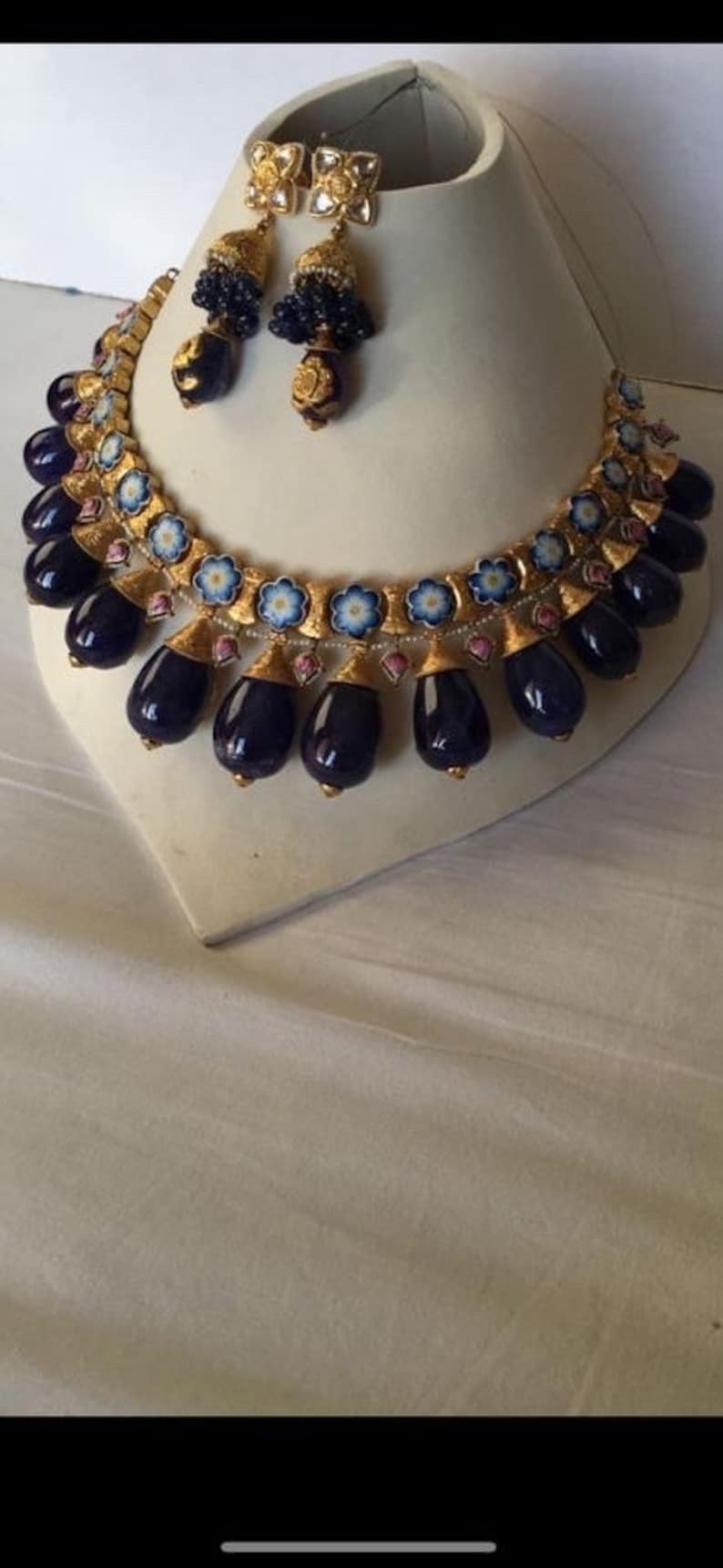 Pu&ograve; includere: Una collana d'oro con un designo in smalto blu e bianco e perle blu scuro a forma di lacrima. La collana &egrave; abbinata a orecchini abbinati con un design simile.