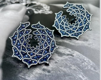 Op de afbeelding: Een paar grote, ronde oorbellen met een delicaat, ingewikkeld ontwerp. De oorbellen zijn gemaakt van zilver en zijn bezet met honderden kleine blauwe saffieren.