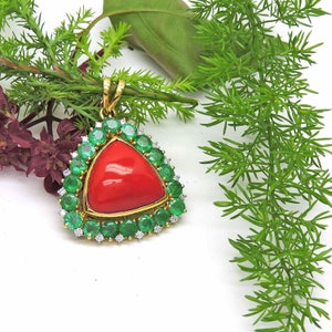 May include: A triangular pendant featuring a large red coral gemstone, encircled by a halo of green emeralds and small diamonds.