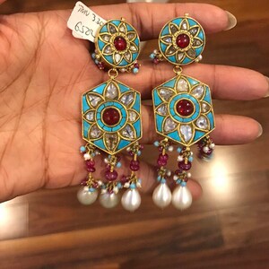 May include: A pair of gold earrings with turquoise and red stones, and pearl drops. The earrings have a hexagonal shape with a floral design in the center. The text "R252 330 MM" is visible on the tag.