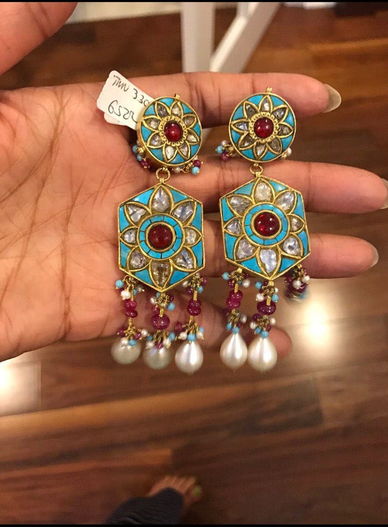 May include: A pair of gold earrings with turquoise and red stones, and pearl drops. The earrings have a hexagonal shape with a floral design in the center. The text "R252 330 MM" is visible on the tag.