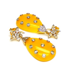 May include: A pair of yellow teardrop-shaped earrings with a star-shaped diamond cluster at the top and smaller diamonds scattered across the teardrop.